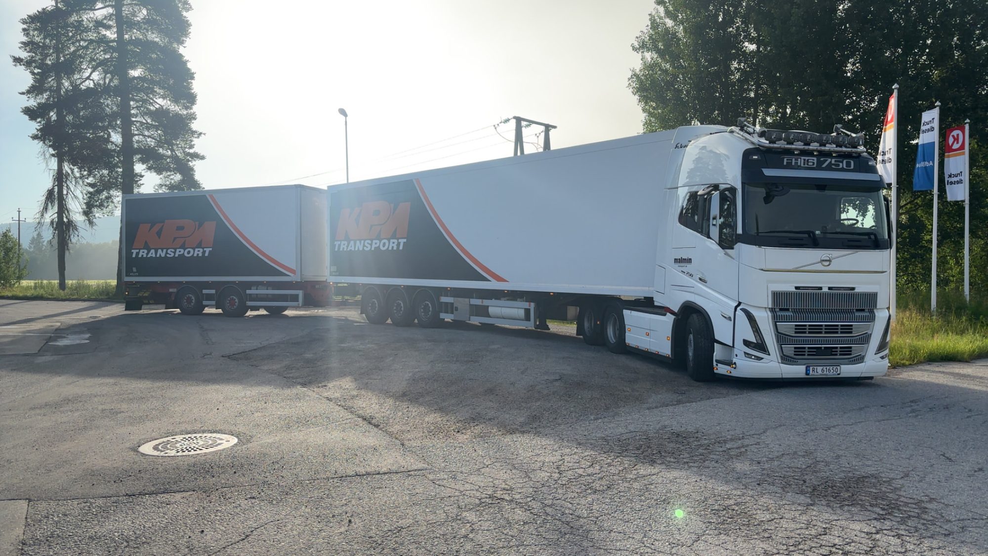 Semitrailer med hvit trekkvogn og kjølehenger parkert på et industriområde i kveldssol.